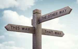 繁體中文 (Traditional Chinese) 一個木製十字路標的三個指示牌上分別寫著「THIS WAY」（這條路）、「THAT WAY」（那條路）與「THE OTHER WAY」（另一條路），背景為晴朗的藍天白雲，生動詮釋海內外醫學系申請者在進行醫學院選校時面臨的多重路徑抉擇。 簡體中文 (Simplified Chinese) 一个木制十字路标三个指示牌上分别写着「THIS WAY」（这条路）、「THAT WAY」（那条路）与「THE OTHER WAY」（另一条路），背景为晴朗的蓝天白云，生动诠释海内外医学系申请者在进行医学院选校时面临的多重路径抉择。 英文 (English) A wooden directional signpost pointing three different ways with text "THIS WAY", "THAT WAY", and "THE OTHER WAY" against a sky background, illustrating an applicant's decision-making process when choosing between different medical schools or university career paths.